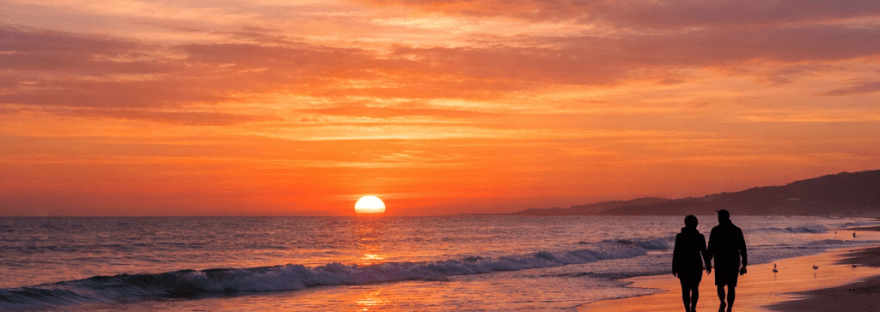 Silhouetted couple walking on beach during orange sunset